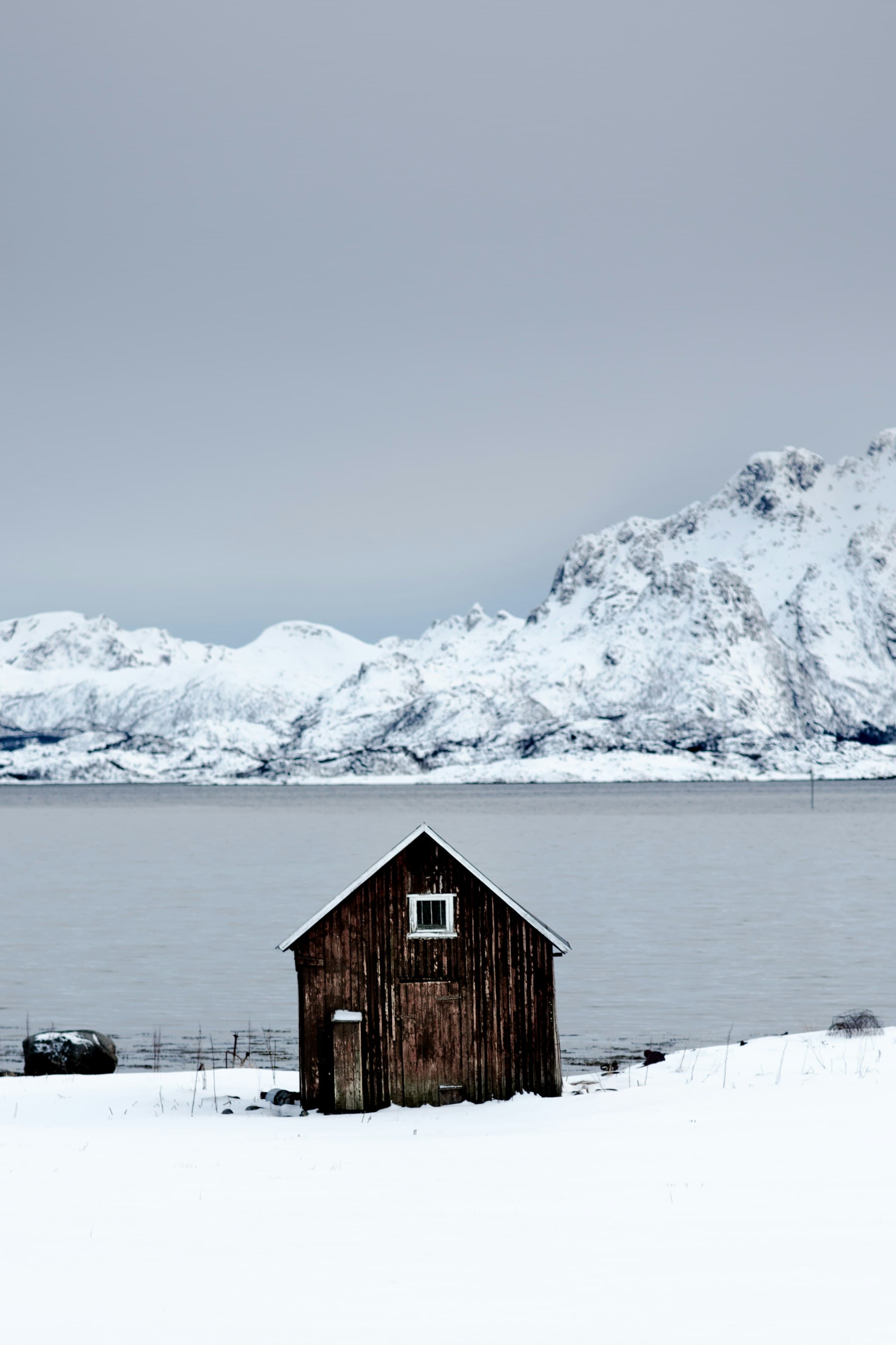 A wooden cabin by a lake below snowy mountains